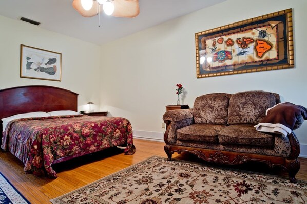A bedroom with a wooden bed, a floral bedspread, a patterned sofa, a rug, and a map on the wall.