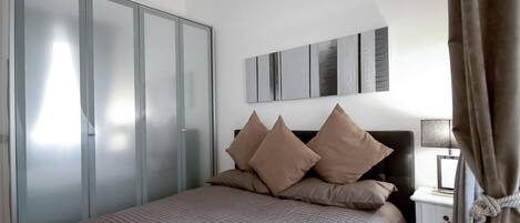 A bedroom with a bed, a wardrobe, a nightstand, and a lamp.