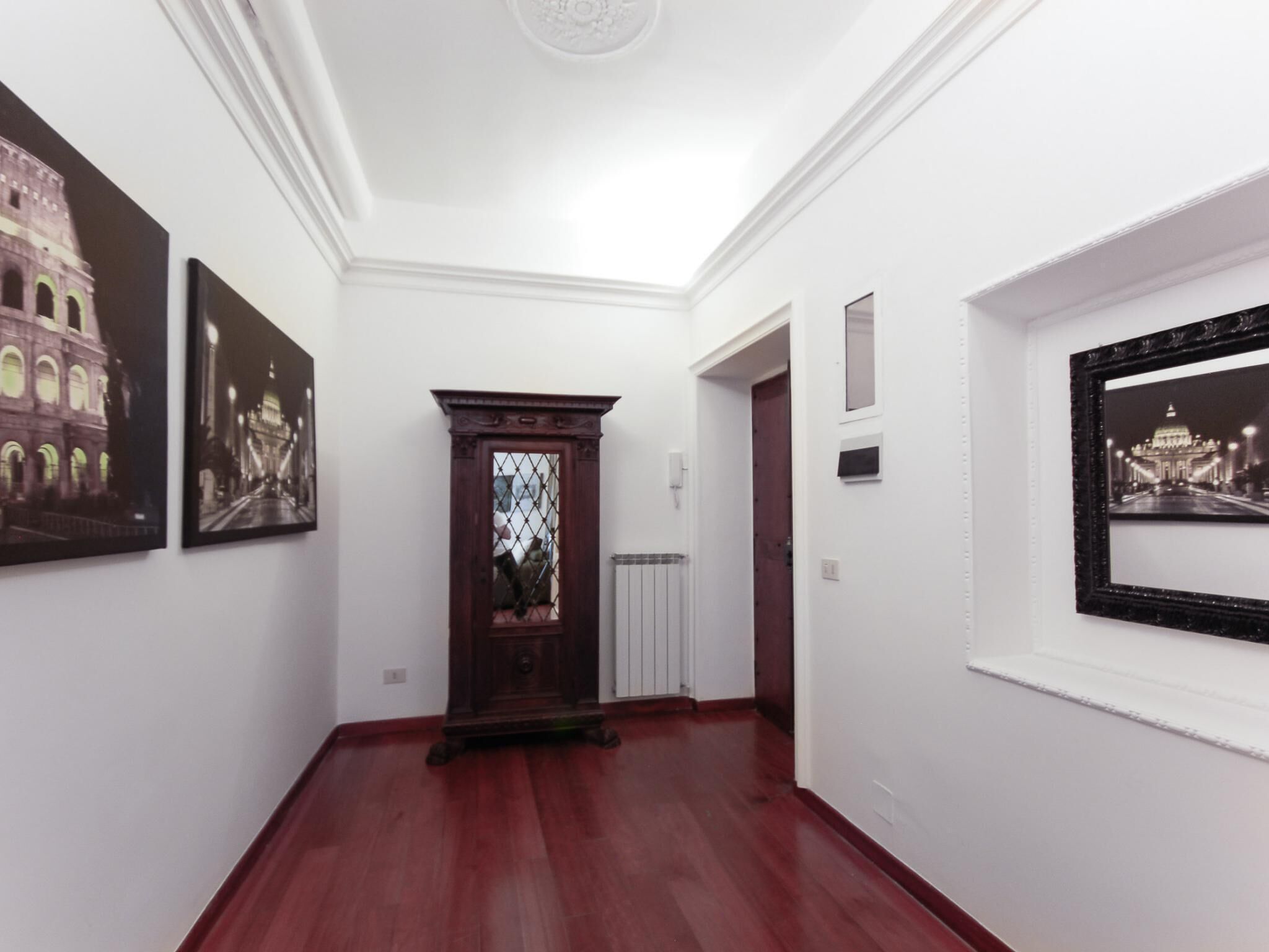 Un couloir doté d’un plancher en bois, de murs blancs et de tableaux encadrés représentant des monuments architecturaux.