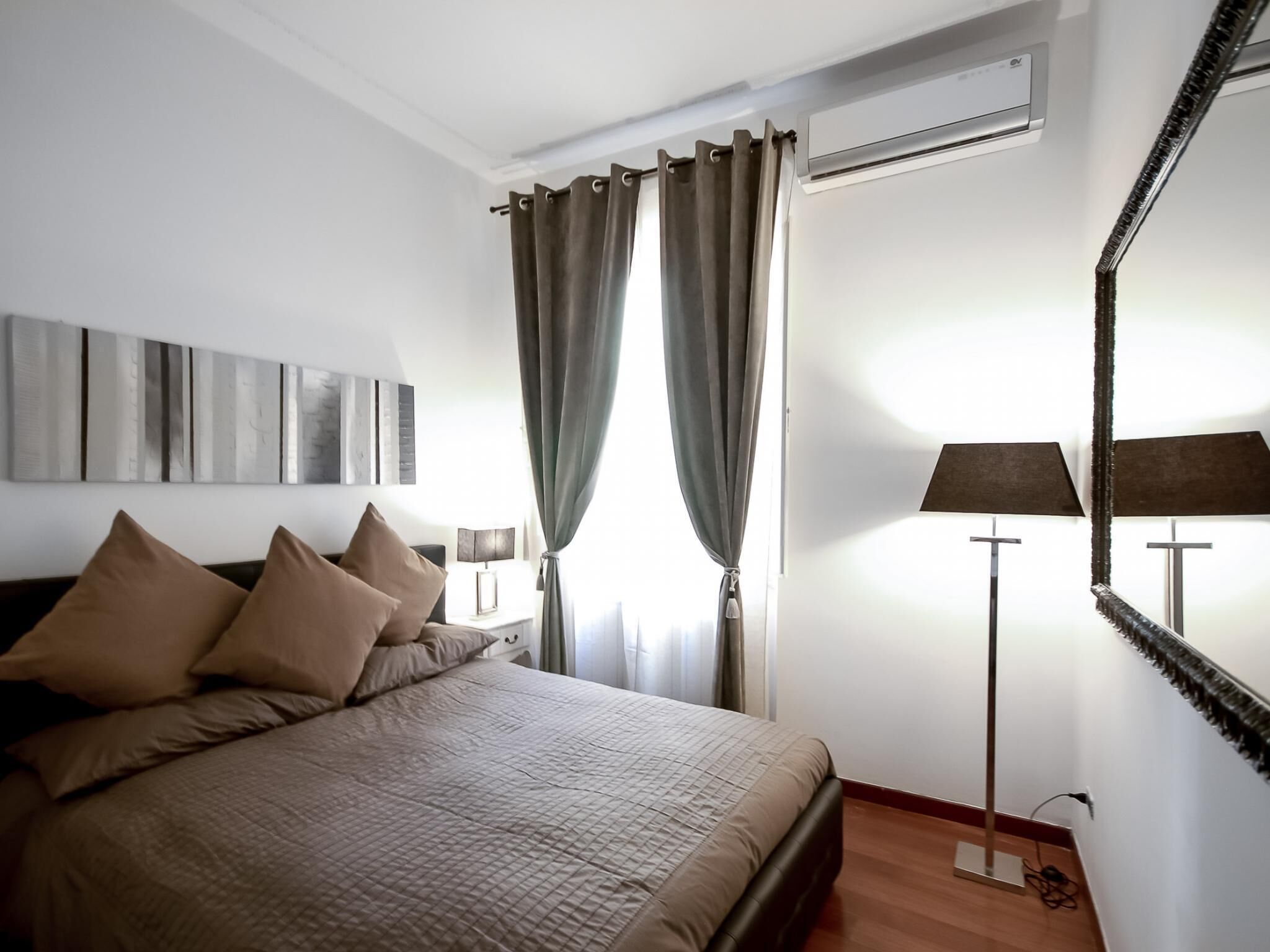 A bedroom with a bed, curtains, a lamp, and a mirror.