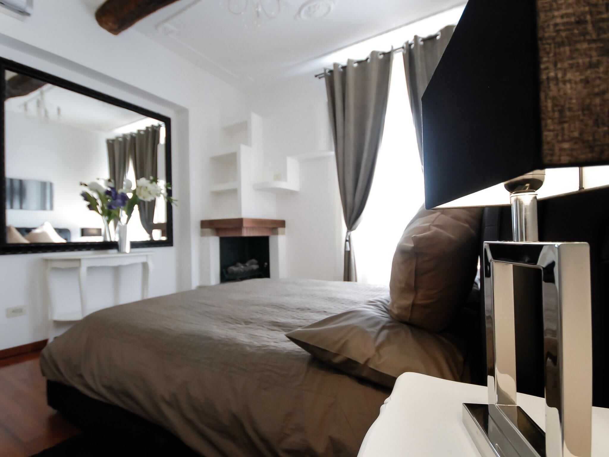 A modern bedroom with a large bed, a flat-screen TV, a fireplace, and a mirror.