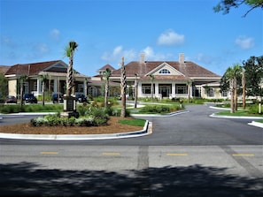 Un quartier résidentiel avec un panneau indiquant la présence d’un club de golf, des palmiers et une allée sinueuse menant à une maison dont le toit est recouvert de tuiles.