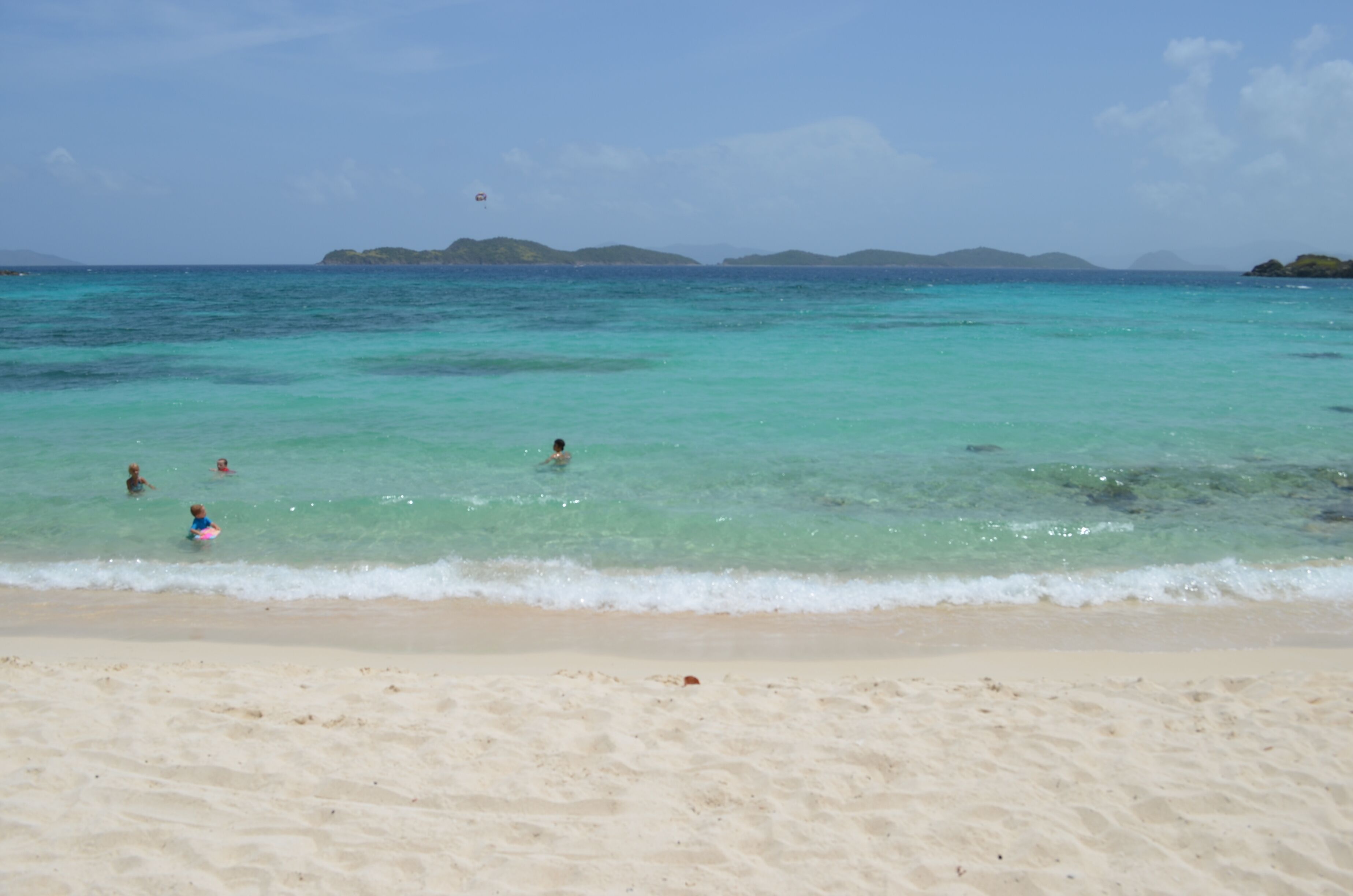 Una playa con aguas turquesas cristalinas, orilla de arena y islas a lo lejos.