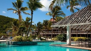Une piscine à l’eau d’un bleu limpide, entourée de palmiers et bordée d’un bâtiment dont le toit est recouvert de tuiles.