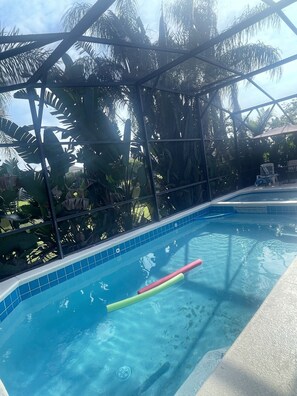 Une piscine à l’eau d’un bleu cristallin, entourée d’une clôture en métal et d’une végétation tropicale luxuriante.