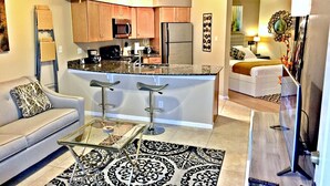 A modern kitchen with a central island, bar stools, a sofa, and a glass coffee table. - Splendid, Tastful, And Fully Furnished Condo On Lake Travis Island Villa!!! (Lago Vista)