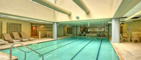 An indoor swimming pool with clear lanes, lounge chairs, and a high ceiling with skylights.