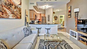 A modern living room with a sofa, a glass coffee table, and a kitchen in the background. - Splendid, Tastful, And Fully Furnished Condo On Lake Travis Island Villa!!! (Lago Vista)