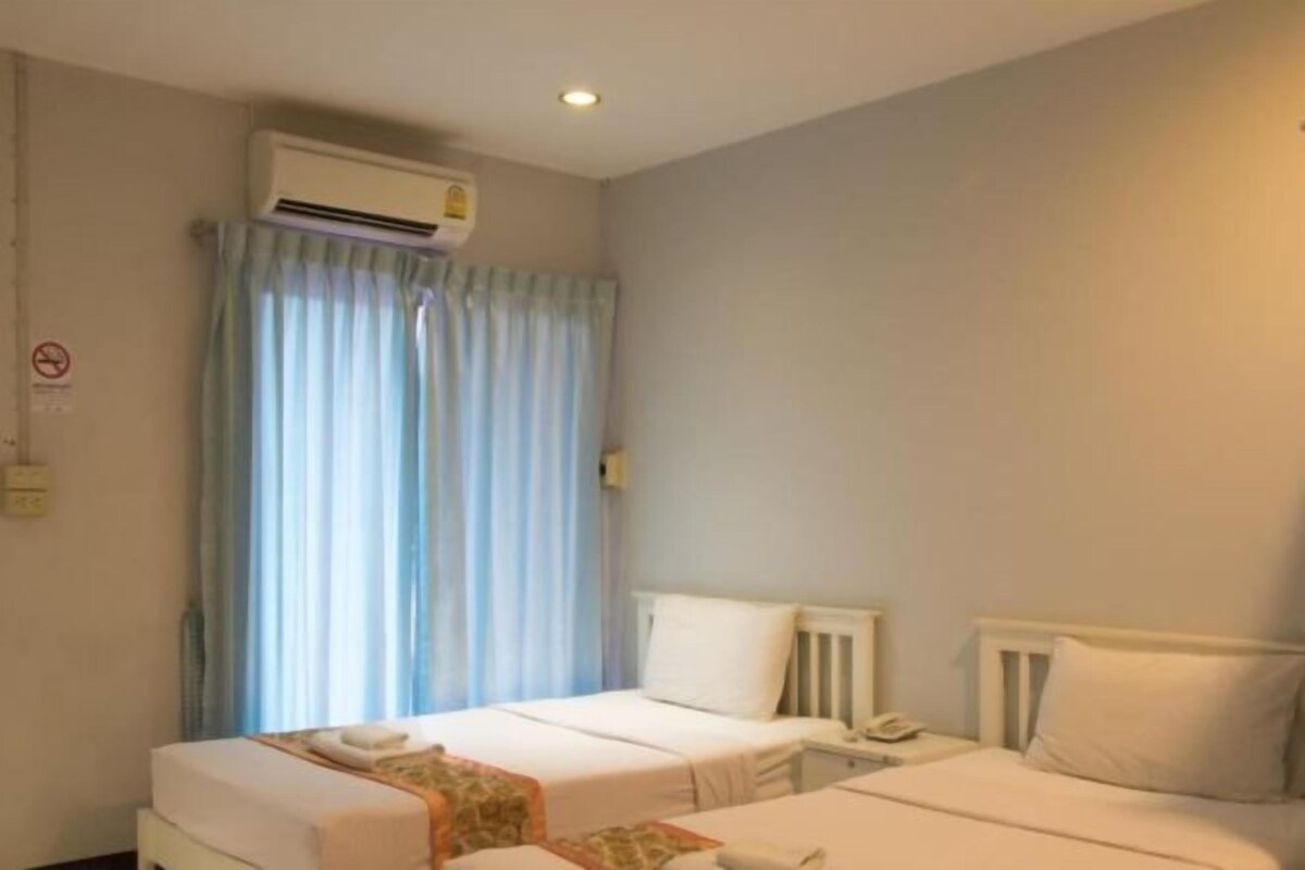 Habitación de hotel con dos camas, una ventana con cortinas, un aire acondicionado y un teléfono en la mesita de noche.