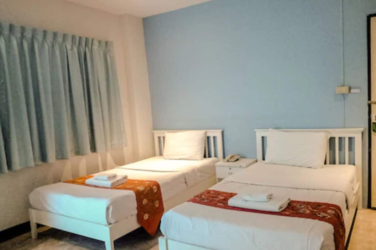 A hotel room with two single beds, a small bedside table with a phone, and a window with curtains.