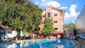 A swimming pool with a clear blue water surface, surrounded by trees and a building with multiple windows and balconies. - NIM SEE SENG Hotel (Chiang Mai)