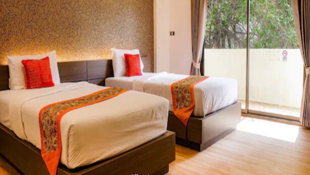A hotel room with two beds, a patterned wall, and a large window with curtains. - NIM SEE SENG Hotel (Chiang Mai)