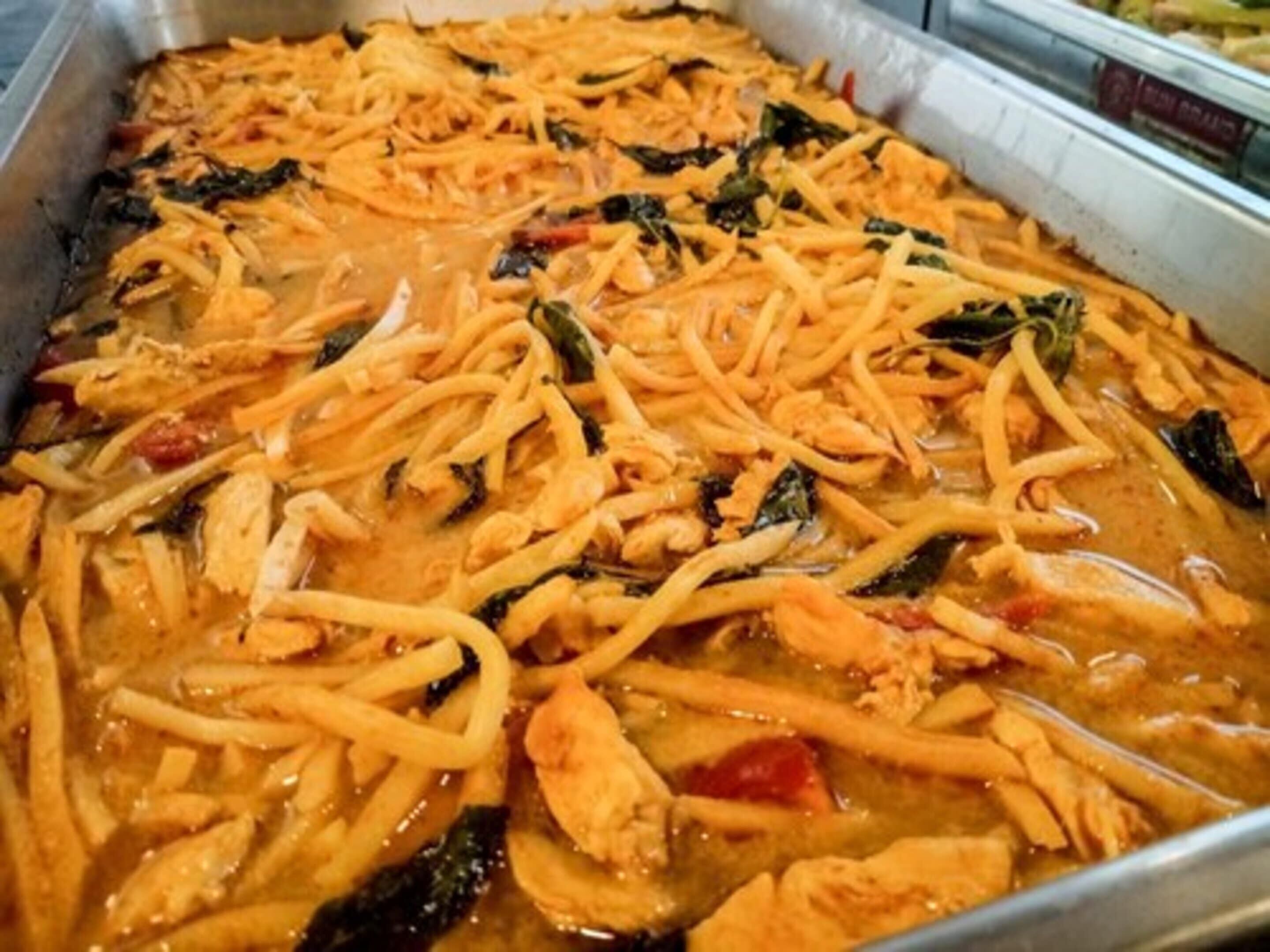A tray of food with noodles, vegetables, and chicken in a sauce.