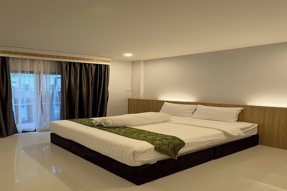 A modern hotel room with a large bed, a wooden headboard, and a view of the outside through a window with curtains.