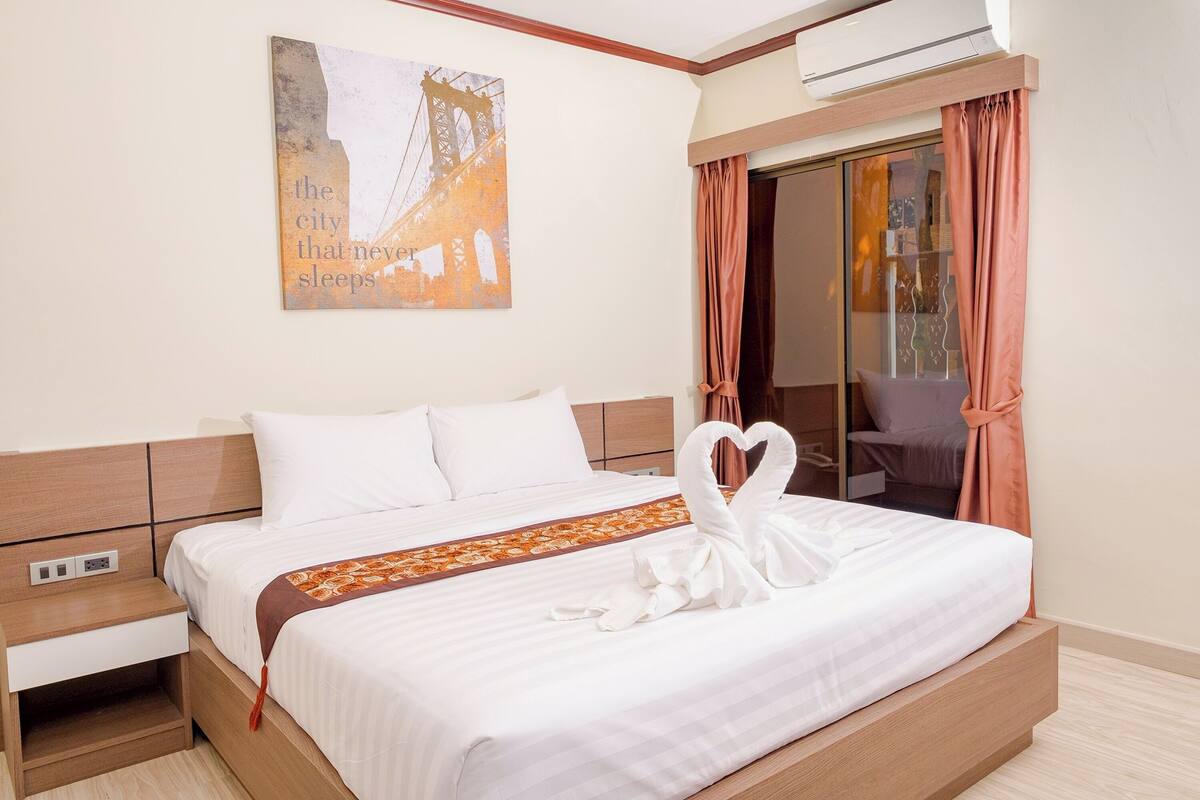 A neatly made bed with a decorative swan towel, a wall-mounted artwork, and a sliding glass door with curtains.