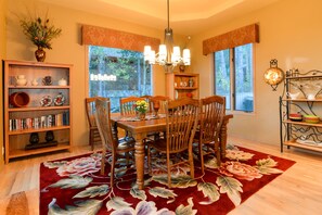 A dining room with a wooden table and chairs, surrounded by bookshelves and a floral rug.