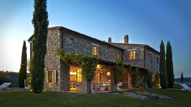 A stone house with a patio, outdoor seating, and tall trees.
