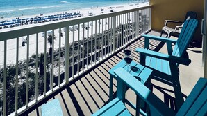 Ein Balkon mit Blick auf Strand und Steg, ausgestattet mit blauen Adirondack-Stühlen und einem Tisch mit einem Glas Wein.