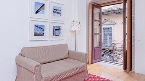 A room with a beige sofa, a red rug, and a balcony with a metal railing. - Flowerstreet54 - Romantic Apartment at Downtown Center (Porto)
