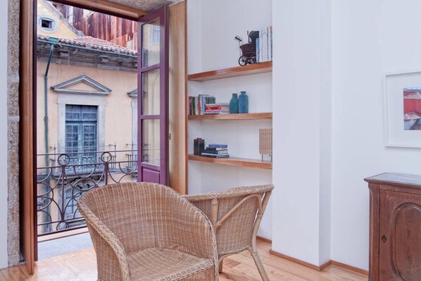 A balcony with wicker chairs, a wooden bookshelf, and a small cabinet.