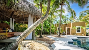 Un complexe hôtelier tropical doté d’une piscine, de palmiers et d’une structure à toit de chaume.