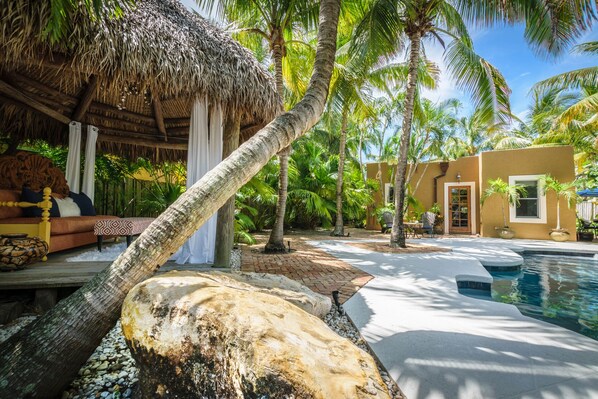 Um resort tropical com piscina, palmeiras e uma estrutura de telhado de palha.