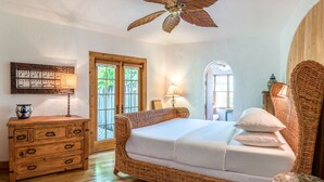 Une chambre à coucher avec un grand lit, une commode en bois, des meubles en osier et un ventilateur de plafond.
