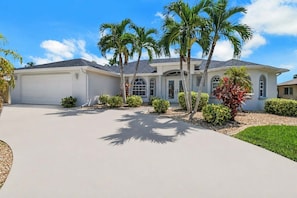 A two-story house with a garage, surrounded by palm trees and well-maintained landscaping.