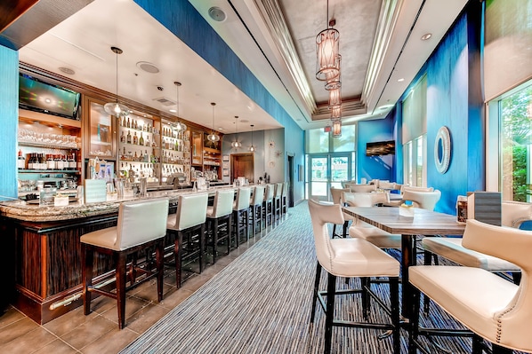 A bar area with a long counter, multiple bar stools, and a television screen. - MGM Signature 33rd floor 3BR4BA PH StripView-Balcony-NO Resort fee-FREE Parking (Las Vegas)
