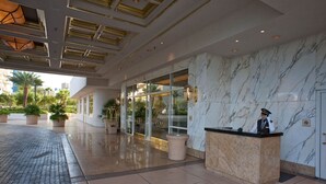Eine Hotelhalle mit einer Marmorrezeption, einem Concierge und einem Glastür-Eingang.