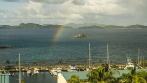 Ein Yachthafen mit vertäuten Booten, ein klarer Himmel und eine entfernte Insel mit einem Regenbogen.