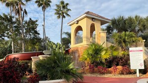 A building with a red roof and arched entrance, surrounded by tropical plants and palm trees. - TROPICAL RESORT! 3 Pools, Lazy River, Water Slide +more!  4 BED/3 BATH (Davenport)