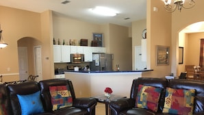 A living room with leather sofas, a coffee table, and a kitchen in the background. - 5*Luxury Villa 6BR,4BA 3Ensuits /Pool facing SE/10mins to Disney parks,free Wifi (Kissimmee)