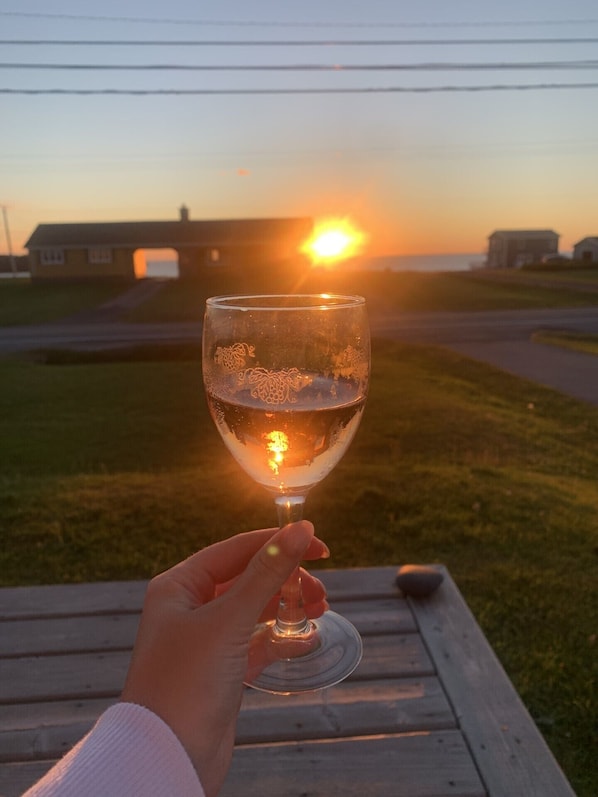 Käsi, jossa on viinilasi, ja taustalla auringonlasku.