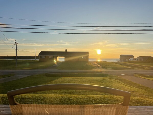 Una casa con un arco grande al atardecer, un campo cubierto de hierba y una masa de agua al fondo.