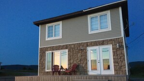 Une maison à deux étages avec une façade en pierre, de grandes fenêtres et un porche couvert avec des chaises.