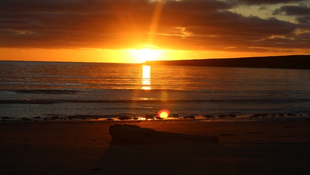 Un coucher de soleil sur une plage, avec une formation rocheuse au premier plan.