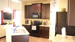 A modern kitchen with dark wooden cabinets, a black microwave, a stove, and a refrigerator. - Beautiful & Cozy, BMT Friendly near SeaWorld 3mi/Six Flags 14mi/Lackland 8mi (San Antonio)
