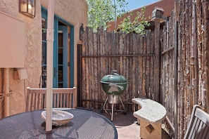 A patio with a round metal table, a stone bench, and a green barbecue grill. - Railyard Adobe, Walk to the Plaza (Santa Fe)