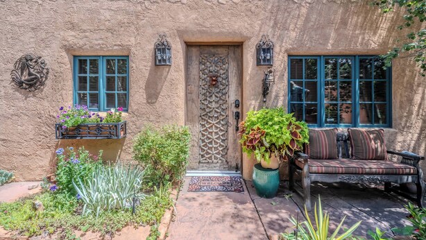 A rustic building with a textured facade, a wooden door with a geometric pattern, and a bench with cushions outside.
