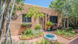 A rustic building with a stucco exterior, a small garden with various plants and a birdbath, and a bench with a potted plant.