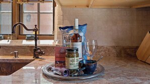 A kitchen counter with a bottle of wine, a can of salsa, a glass, a bag of chips, and a metal tray with utensils.