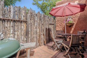 A rustic outdoor patio with a wooden fence, a green gas grill, and a table with chairs. - Railyard Adobe, Walk to the Plaza (Santa Fe)