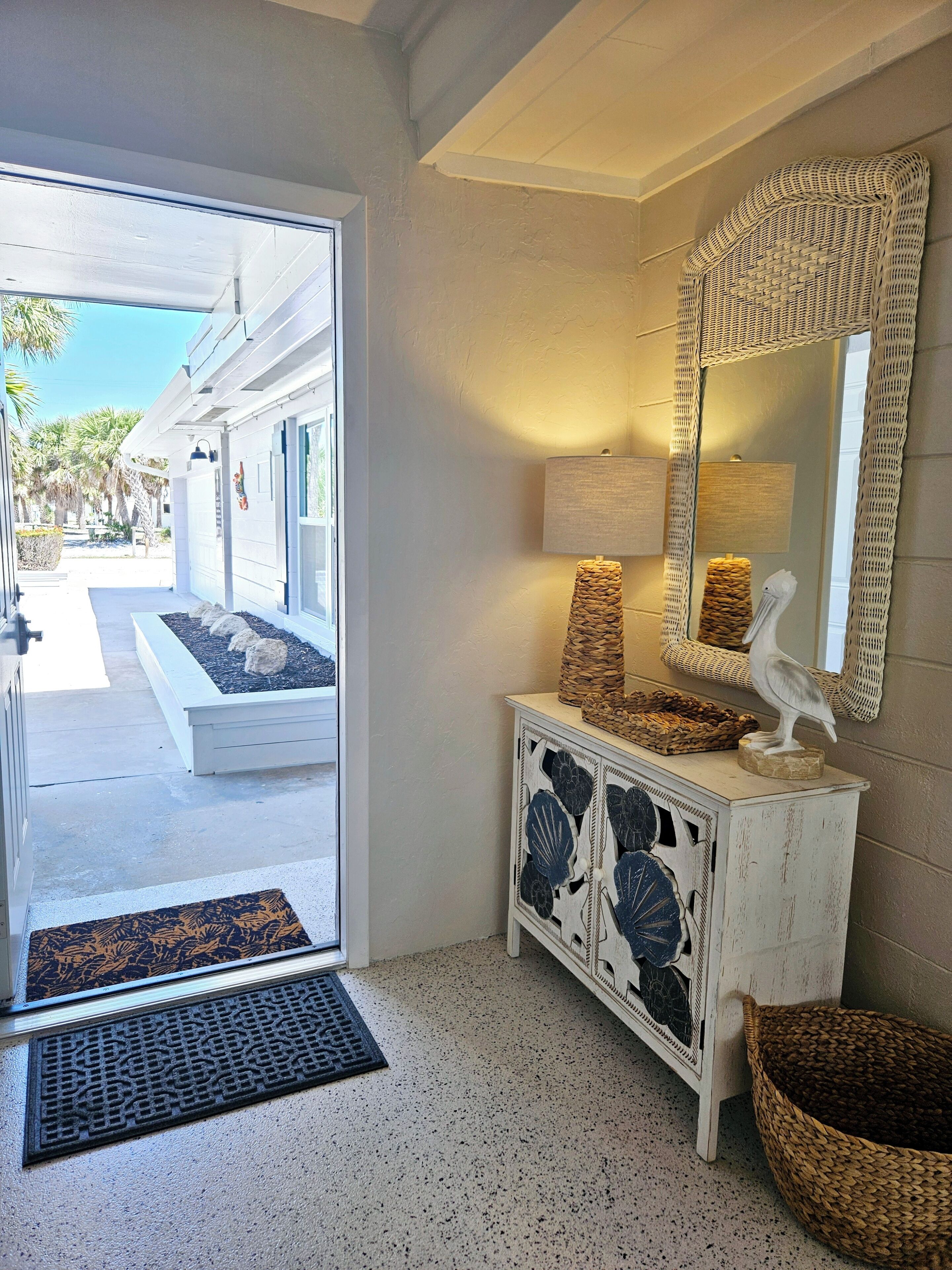 A room with a white console table, a woven mirror, and a decorative bird statue.