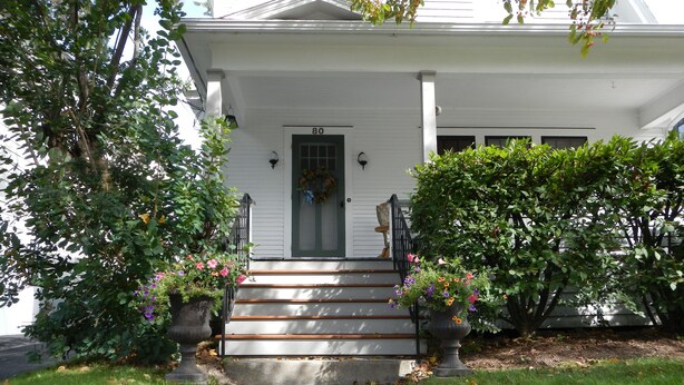 A white house with a green door, numbered 80, and a front porch with steps leading to the entrance.
