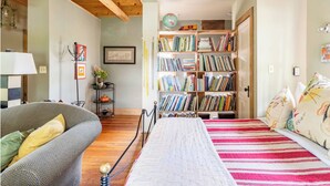 Una habitación acogedora con sofá, cama con ropa de cama a rayas, estantería llena de libros y un globo en el techo.