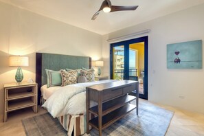 A bedroom with a bed, bedside tables, a desk, a ceiling fan, and a view through an open door.
