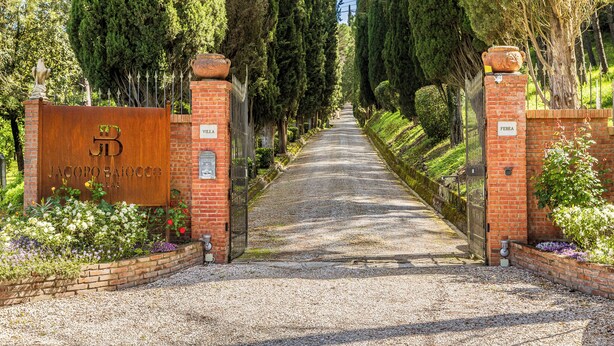 Un sendero de grava conduce a una entrada con puerta y un letrero que dice 'Jacopo Baiocco Villas'.