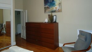 A room with a wooden dresser, a gray armchair, and a painting on the wall. - Down Town Heritage Suite on Water Street           (Charlottetown)