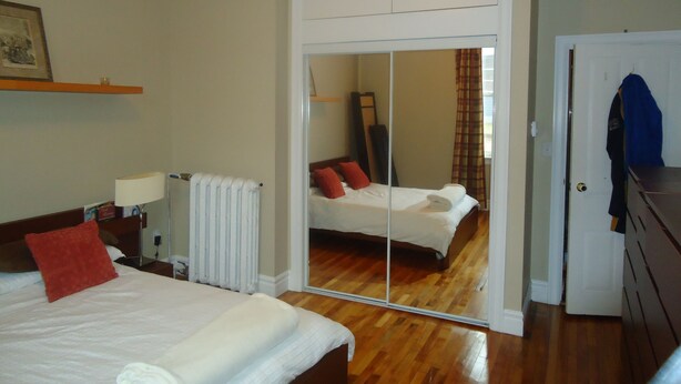A hotel room with a bed, a mirror, a dresser, and a door. - Down Town Heritage Suite on Water Street           (Charlottetown)